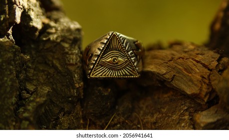 Vintage silver ring depicting an all-seeing eye in a triangle on an old wood background and a blurred yellow-green background