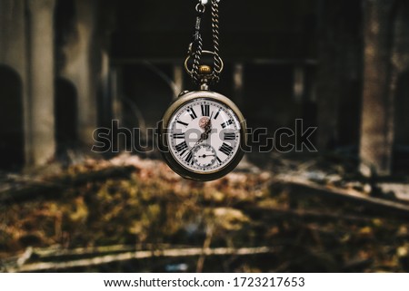 Vintage silver watch with chainlet hanging over the ruins of the cathedral. The wind of time concept.