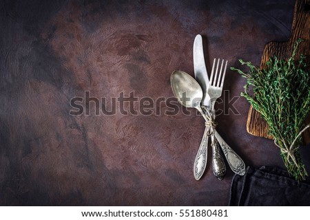Vintage silverware on a dark textile and bunch of fresh thyme on dark rusty background. Top view, copy space for text.