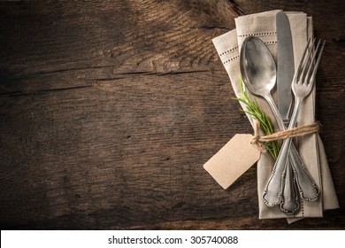 Vintage silverware with a twig of rosemary and empty tag on rustic wooden background