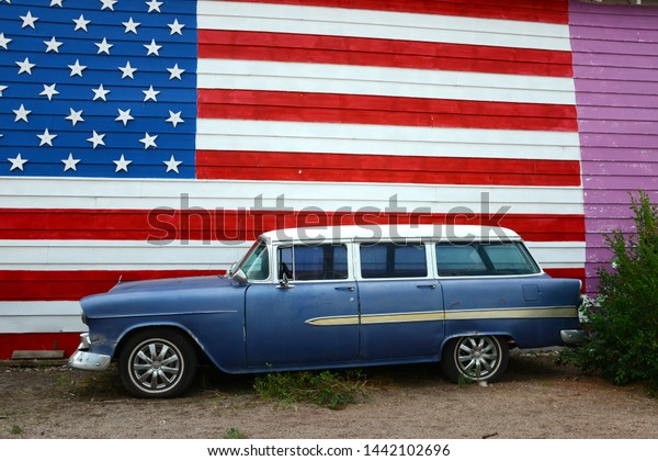 vintage station wagon parked in front of wall with\
painting of american\
flag