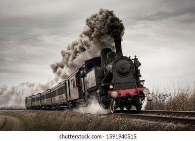 Vintage steam train with ancient locomotive and old carriages runs on the tracks in the countryside