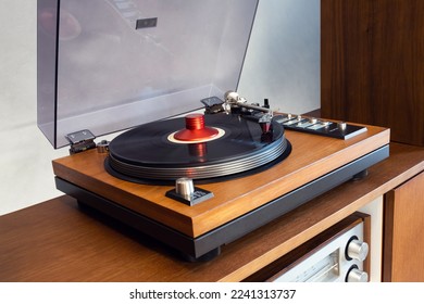 Vintage Stereo Turntable Vinyl Record Player with Open Plastic Lid and Wooden Plinth Standing Above Amplifier. Home Retro Audio Sound Equipment.