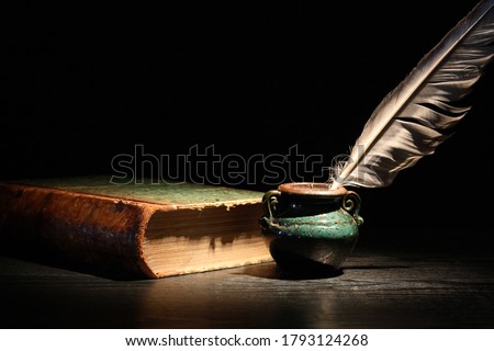 Vintage still life with old book and quill pen on dark background