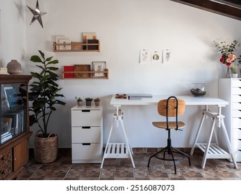 A vintage studio with a white desk, a chair, books, art prints, plants and wooden beams. The desk is complemented by white drawers and shelves, creating a rustic and cozy ambiance throughout the room. - Powered by Shutterstock