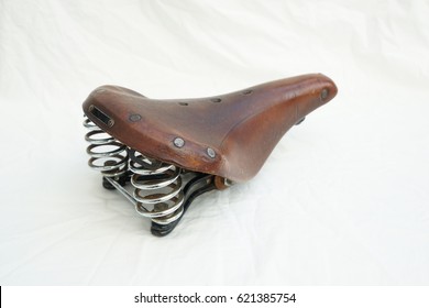 vintage style brown leather bicycle saddle with metal springs on structured white background