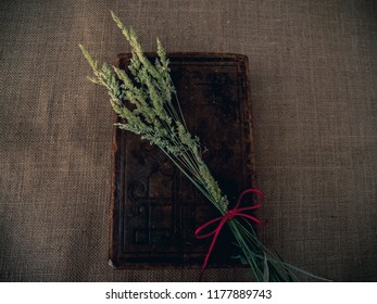 Vintage Style. Closed Antique Book With Dry Grass And Red Thread With Burlap Background