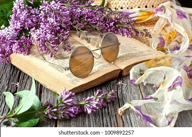 Vintage style composition with lilac flowers, retro book, sun glasses and wicker hat