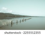Vintage style fence leading into calm blue water of Lake Wairarapa with distant hills across other side in New Zealand North Island.