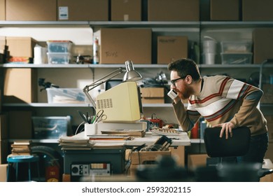 Vintage style nerd using an old computer in the garage and having a phone call with a cordless telephone