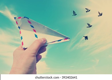 Vintage style photo with hand throwing a paper plane (made of Post envelope) and the flying pigeons against beautiful blue sunny sky