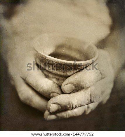 Vintage Style Photo of Man's Worn Hands Holding Cracked Japanese Ceramic Cup. Artistic treatment with texture, toning and grain added for effect. Concept of age, experience and the passing of time.