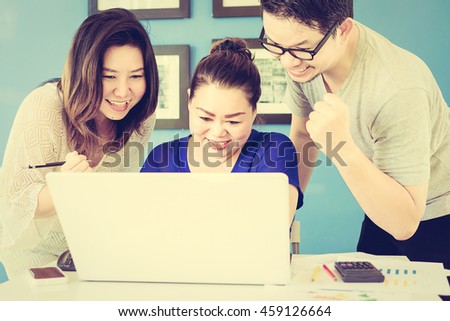 Vintage style photo of two women and one man are happily looking at computer in modern office