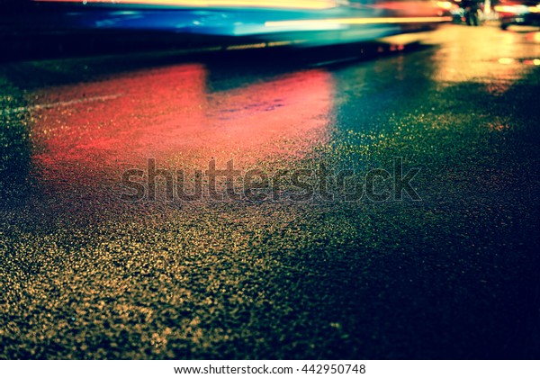 Vintage style - Rainy\
night in the big city, the light from the headlamps of vehicles\
approaching on the road. Close up view from the level of asphalt,\
focus on the asphalt