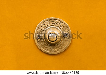Vintage style solid golden brass metal doorbell button against a seamless bright yellow painted wall.