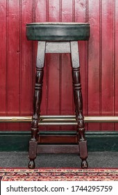 Vintage Style Wooden Pub Stool Against A Dark Red Wooden Bar Shot Straight On.