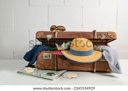 Vintage suitcase packed with travel accessories like straw hat, towels, passport, map and sunglasses for beach holidays in summer, rough white wall, copy space, selected focus, narrow depth of field
