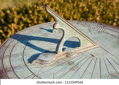 A vintage sundial with green patina throws a long shadow, tracking the motion of the sun while telling the time of day.