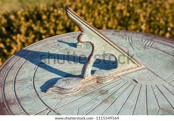 A\
vintage sundial with green patina throws a long shadow, tracking\
the motion of the sun while telling the time of\
day.