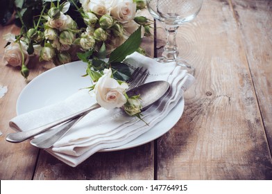Vintage table setting with roses, antique rustic dishes and cutlery on the wooden background, close-up