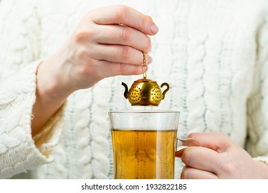 Vintage tea strainer. Woman brews tea with gold tea strainer in the shape of a teapot.