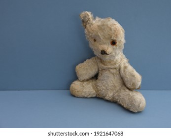 Vintage Teddy Bear In Lovable Play Worn Condition With Missing Eye, Missing Ear And Missing Fur. With Blue Background And Space To Left For Caption. Childhood Memories.