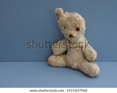 Vintage Teddy bear in lovable play worn condition with missing eye, missing ear and missing fur. With blue background and space to left for caption. Childhood memories.