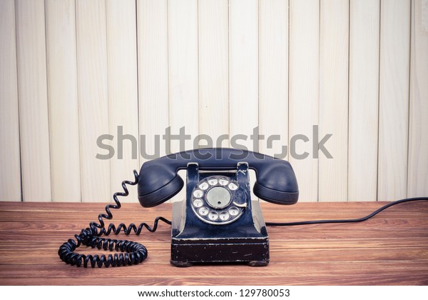 Vintage telephone\
on old table near wood\
wall