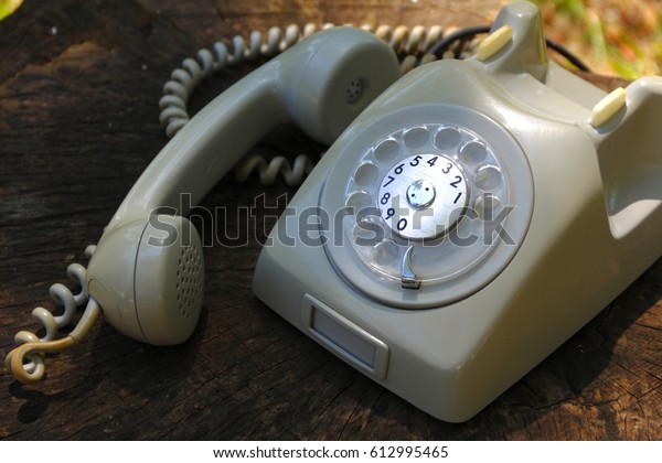 Vintage telephone. Retro beige rotary\
phone over wooden surface with sunset lights       \
