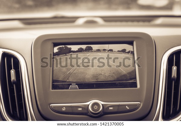 Vintage tone backup\
camera on modern car dashboard with rear view of parking lots in\
America. Automotive rear view system monitor reverse showing motion\
occurrence