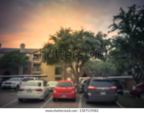 Vintage tone blurred abstract\
apartment complex with detached garage and covered parking lots in\
Texas, America. Row of parked cars under dramatic sunset\
cloud