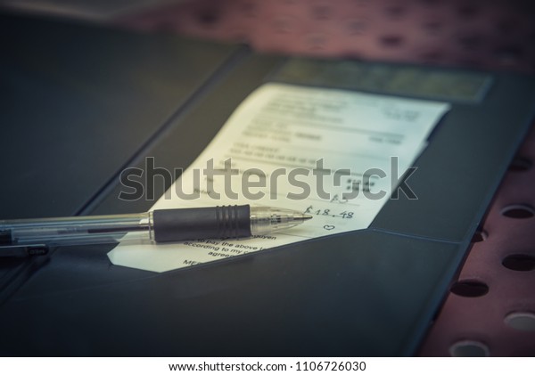 Vintage tone open leather bill holder\
restaurant check, pen. Soft focus receipt hand written total amount\
and tipping on outdoor picnic table, natural light. Paper invoice\
with suggested\
gratuities