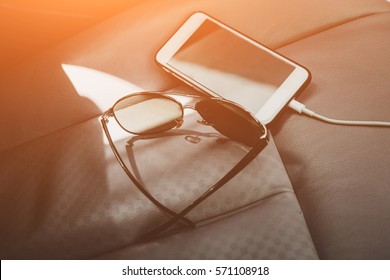 Vintage Tone Picture Of A Battery Charging Smart Phone And Sunglasses On Car Seats