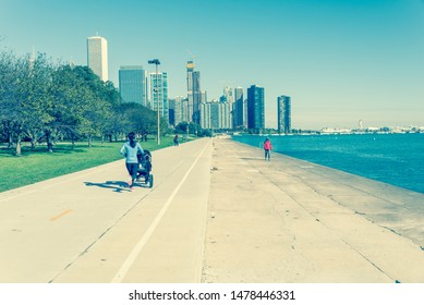 Vintage Tone Rear View Of Fit Asian Lady Running Pushing Stroller Along Shoreline Of Michigan Lake With Downtown Chicago Skylines In Background. Fit Sportswear Woman Exercise Outdoor At Fall Daytime