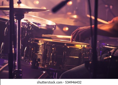 Vintage toned live music background, drummer plays with drumsticks on rock drum set. Closeup photo with soft selective focus
