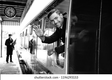 Vintage train arrives at railway station with handsome air force officer in uniform leaning out of window, laughing and waving - Powered by Shutterstock