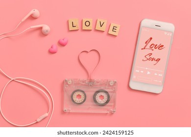 vintage transparent audio cassette magnetic tape in shape of heart, earphones, mobile phone playing love song on screen. flat lay Valentine's Day music on pink background