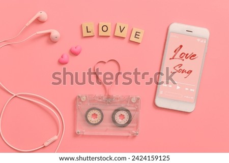 vintage transparent audio cassette magnetic tape in shape of heart, earphones, mobile phone playing love song on screen. flat lay Valentine's Day music on pink background