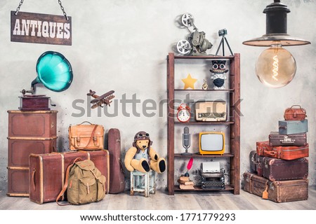 Vintage travel suitcases, backpack, old gramophone, TV, radio, mic, projector, clock, typewriter, quill, books, camera, Teddy Bear, toy plane, signboard, mask. Antiques collectibles. Retro style photo
