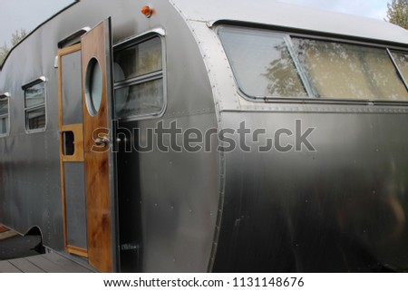 Vintage travel trailer with door open with round window and wood detail.