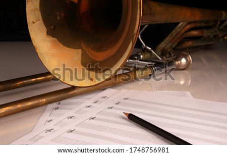 Vintage trombone, pencil and sheet music on a glossy white table and dark background
