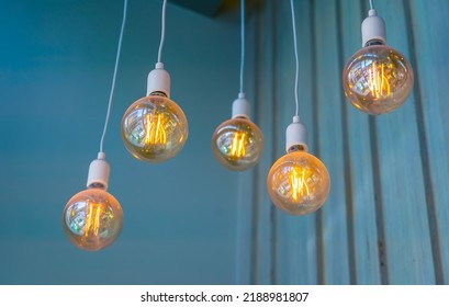 Vintage tungsten filament multiple lamps hanging from the ceiling on a white wires as an interior design concept. Energy and design concept - Shutterstock ID 2188981807