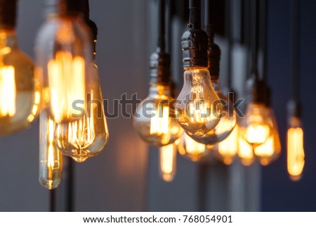 Vintage tungsten filament multiple lamps of different size and style hanging from the ceiling on a black wires as an interior design concept. Energy and design concept