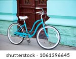 Vintage turquoise bicycle with white elements parked near old building with turquiose walls and brown wooden antique doors.