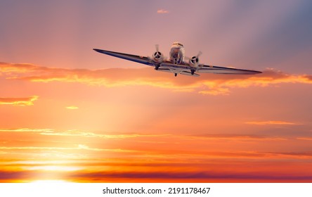 Vintage Type Old Metallic Propeller Airplane In The Sky, Sunset Clouds With Calm Sea In The Background