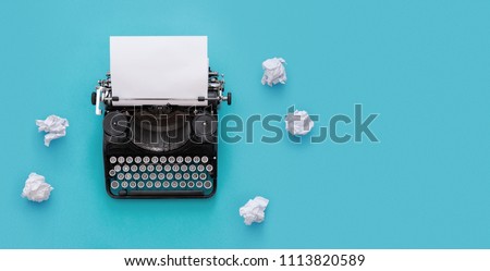 Vintage typewriter and crumpled papers over blue background with copy space