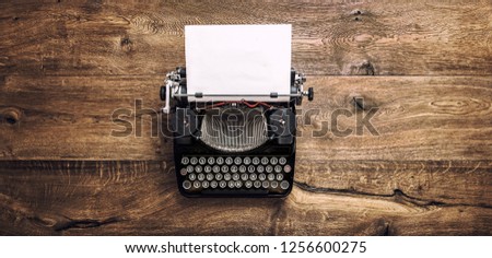 Vintage typewriter with paper page on rustic wooden background. Toned photo