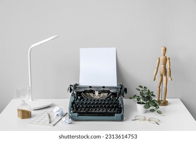 Vintage typewriter with wooden mannequin, lamp and eyeglasses on white table near wall - Powered by Shutterstock