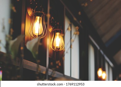 Vintage Wall Lamp Warm Light On Wooden Wall Nand Glass Windows In Cafe And Restaurant With Blurred Image Of Little Flower In Foreground. Vintage Tone Background.