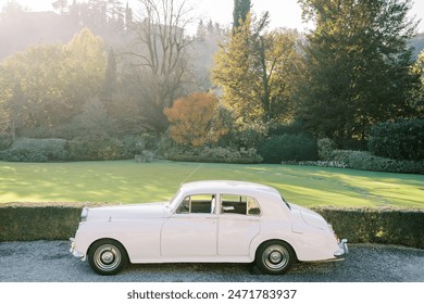 Vintage white Rolls-Royce Silver Cloud stands on a gravel path in a green garden